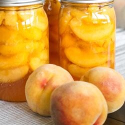 Home canned peaches in glass jars on a kitchen counter with fresh peaches on the side