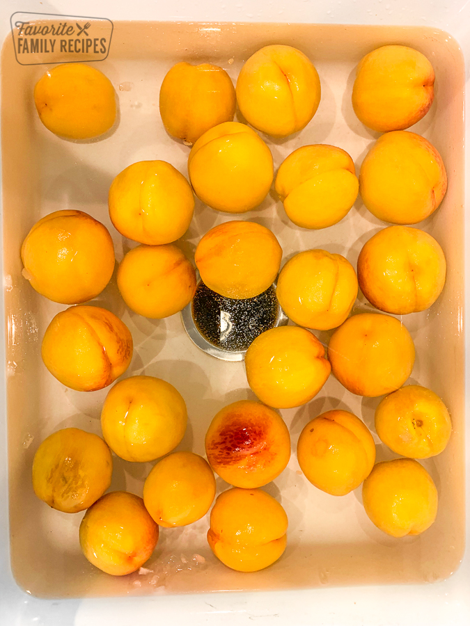 Peaches being prepared for peeling in a sink filled with cold water
