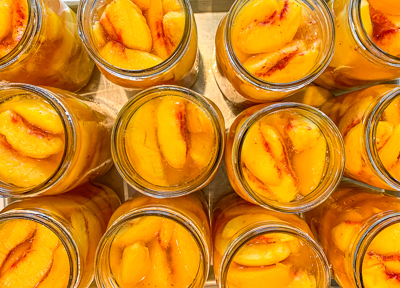 Top view of 12 glass jars with sliced peaches inside.