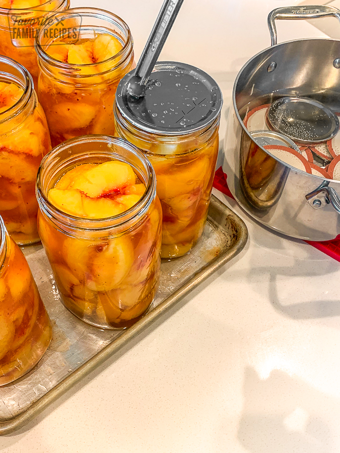 Lids being placed on glass jars filled with peaches for canning