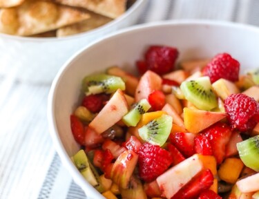 Fruit salsa in a white bowl in front of cinnamon chips in a white bowl.