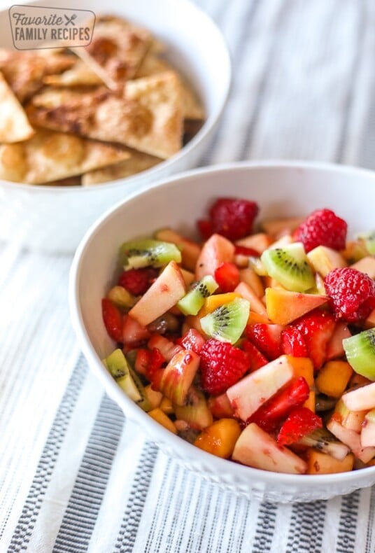 Fruit salsa in a white bowl in front of cinnamon chips in a white bowl.