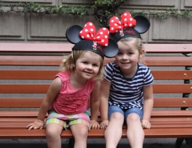 Two little girls with Minnie Ears sitting on a bench at Disneyland