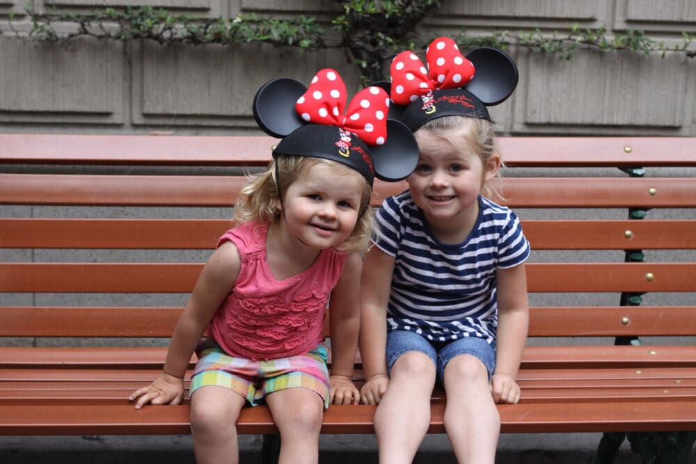 Two little girls with Minnie Ears sitting on a bench at Disneyland