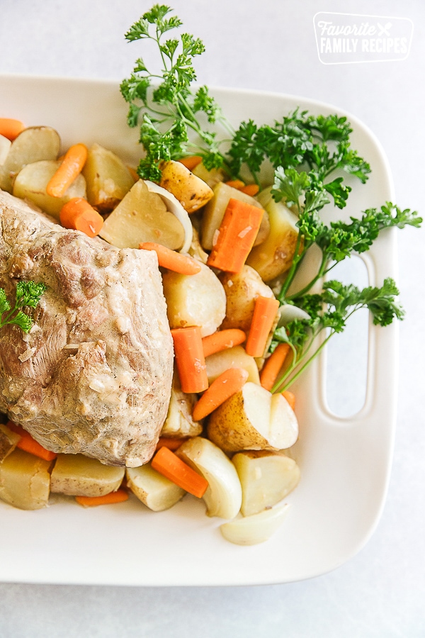 Crock Pot Pork Roast on a white tray with vegetables and a spray of parsley on the side.