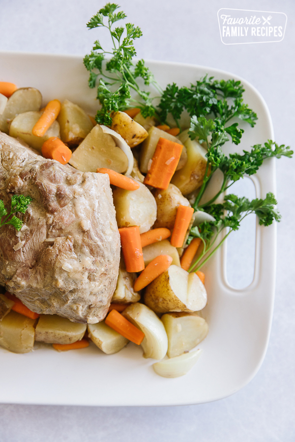 Crock Pot Pork Roast on a white tray with vegetables and a spray of parsley on the side