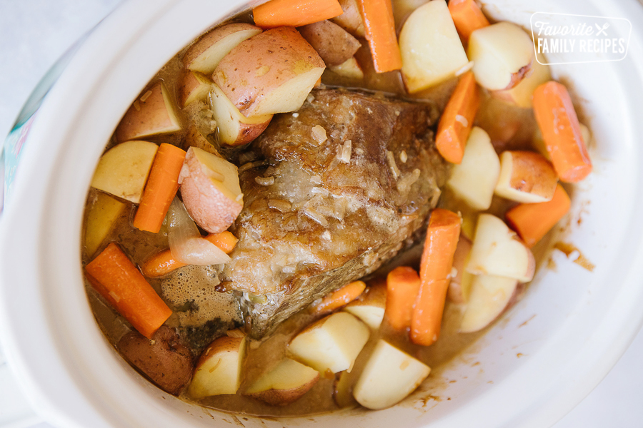 Beef Roast in a white crock pot surrounded by vegetables.