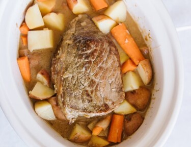 White Crock pot filled with a beef roast, potatoes, carrots, and onions