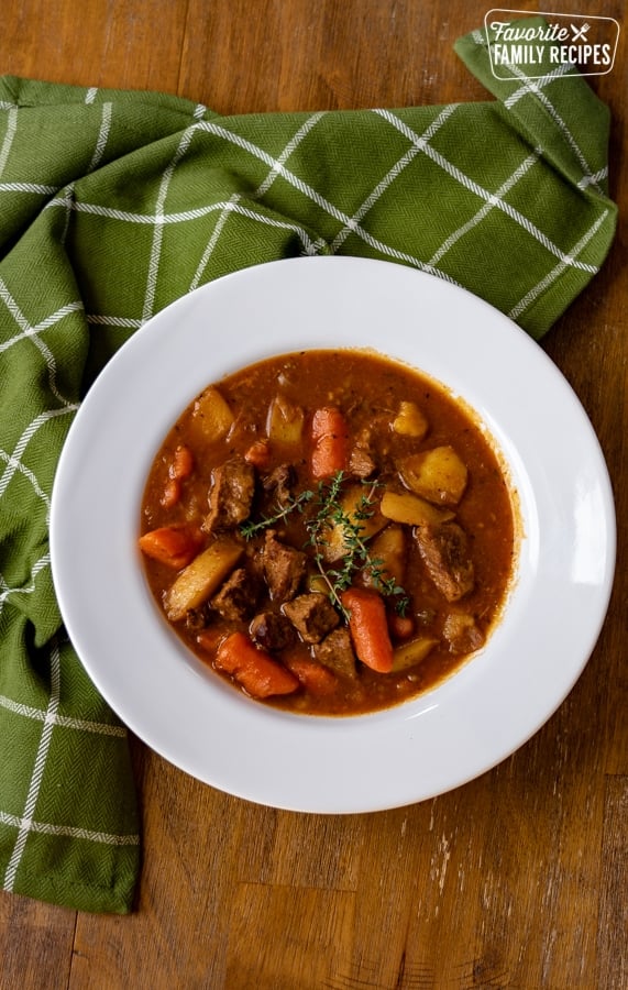 A bowl of instant pot beef stew on a wooden table with a green napkin next to it