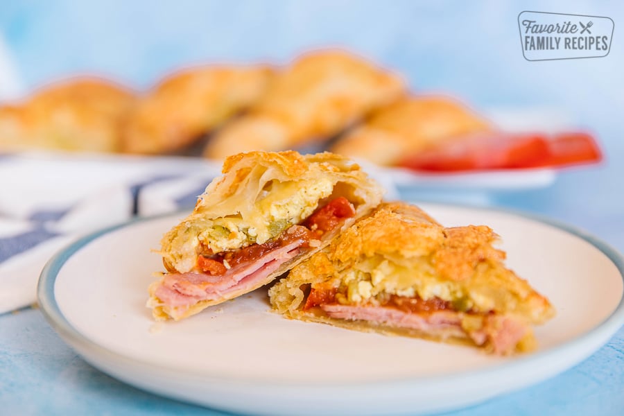 A breakfast hand pie filled with eggs, ham, tomatoes, and green chiles on a blue plate.