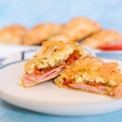 A ham and egg breakfast hand pie on a white plate with a blue background