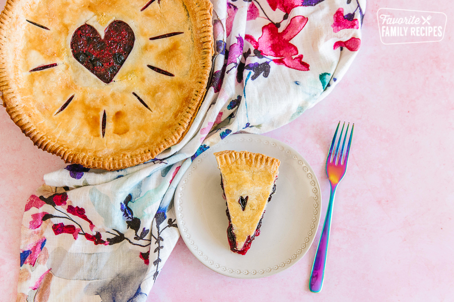 A full berry pie in a pie plate with a slice of pie next to it on a white plate