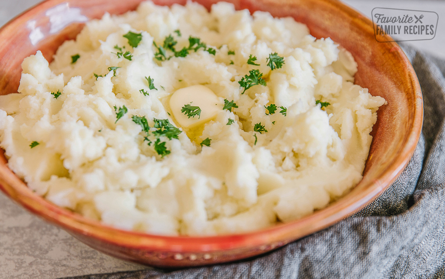Instant Pot Mashed Potatoes in a red bowl with lots of butter and parsley on top.