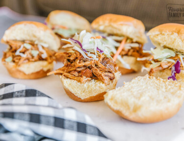 Six instant pot pulled pork sandwiches on a white plate.