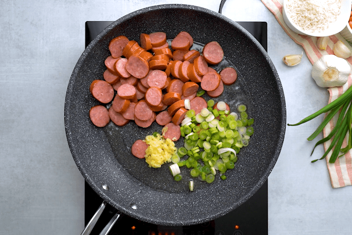 Sausage, green onions, and garlic in a pan for Brazilian Rice and Beans with Sausage.