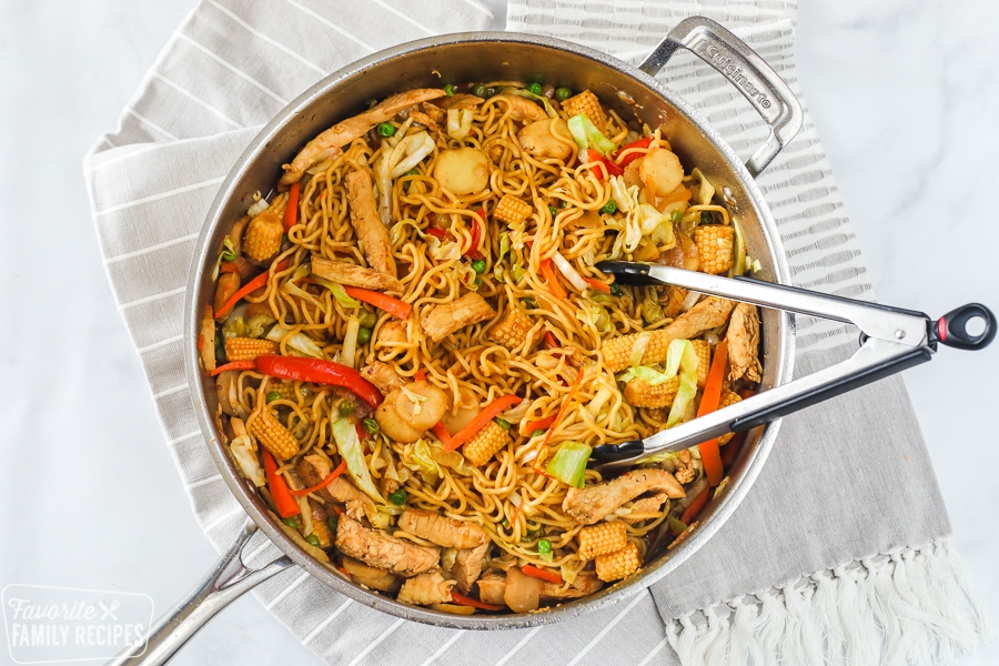 Yakisoba in a skillet with tongs. 