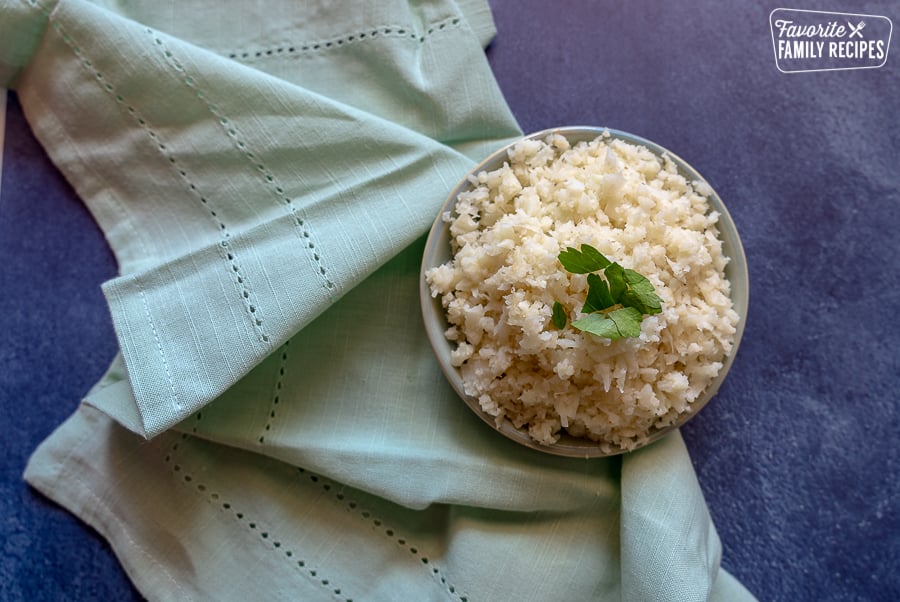Cauliflower Rice is a healthy alternative to rice that comes together in minutes. Use it to sneak more servings of vegetables into all your favorite rice dishes! A bowl of cauliflower rice on a blue background.