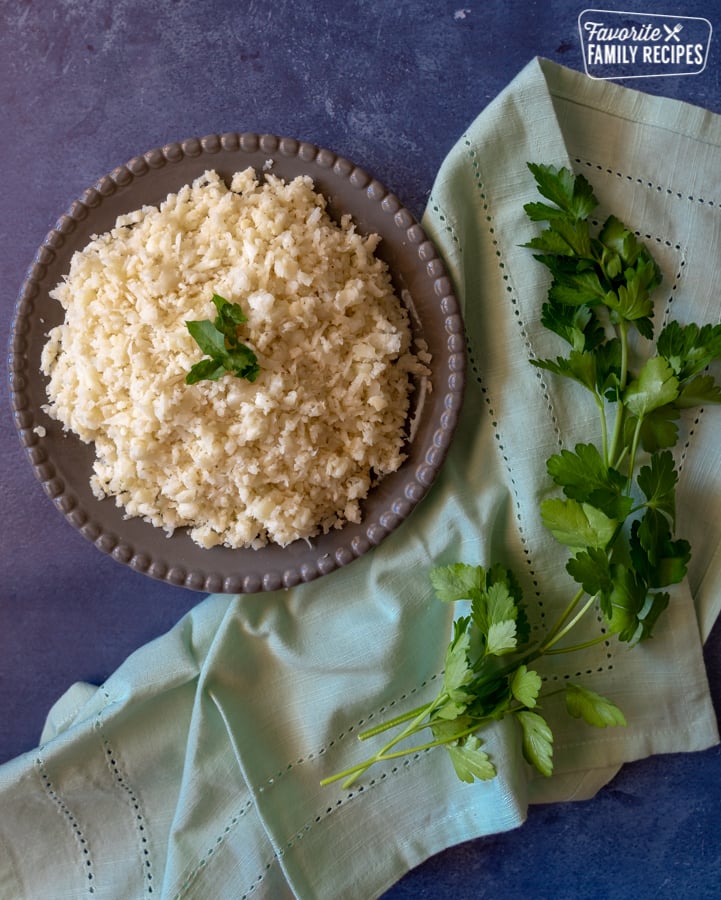 A plate of cauliflower rice on a blue background with parsley scattered around the plate.