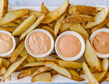 4 varieties of fry sauce on a white tray surrounded by French fries