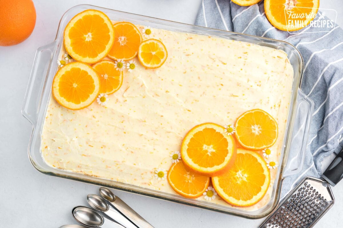 Sunny Yellow Cake with Orange Blossom Frosting in a glass pan topped with orange slices and flowers.