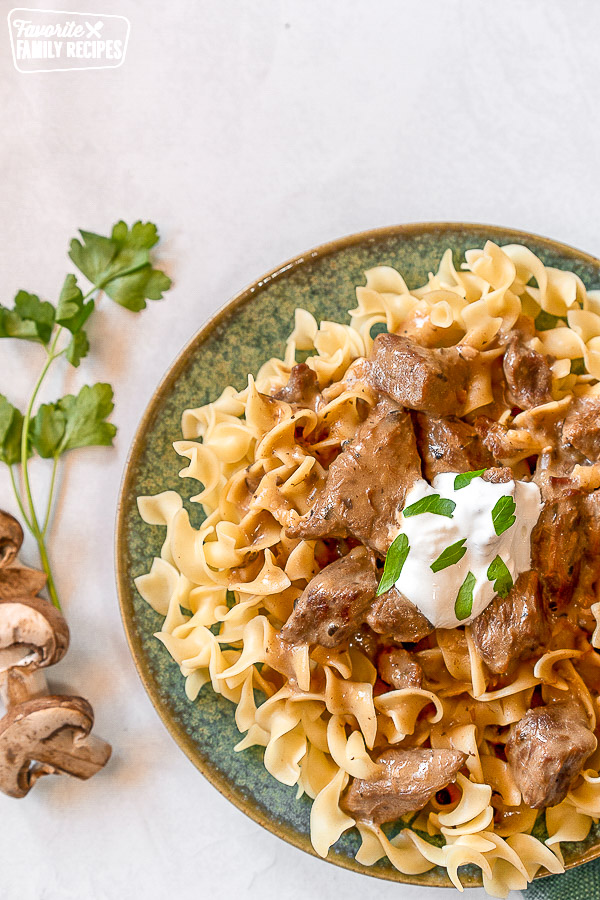 Overhead shot of Beef Stroganoff on a blue plate topped with sour cream and parsley.