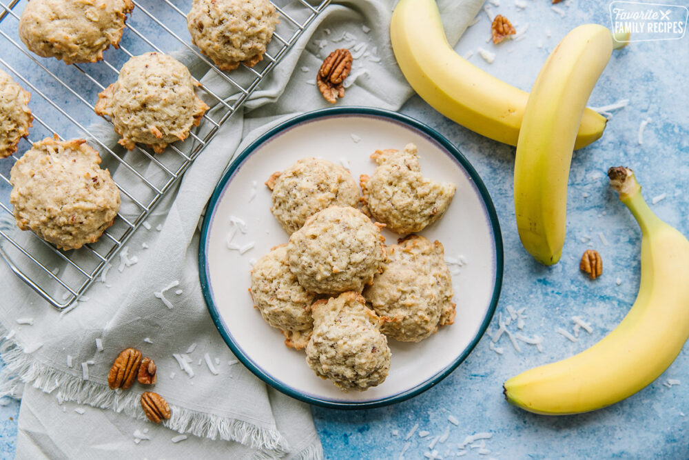 Banana Coconut Delight cookies on a plate, surrounded by pecans and bananas on a blue background.