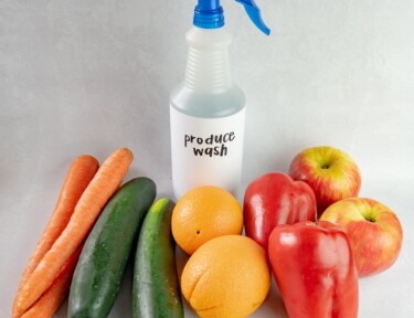 A bottle of produce wash surrounded by fruits and vegetables.