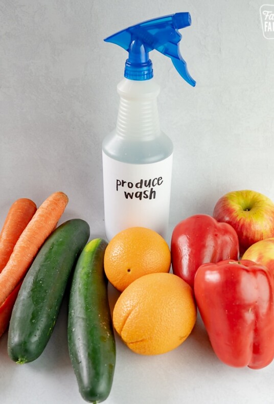 A bottle of produce wash surrounded by fruits and vegetables.