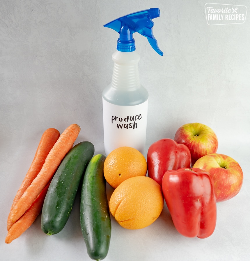 A bottle of produce wash surrounded by fruits and vegetables.