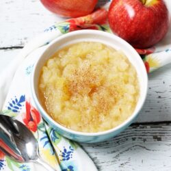 Applesauce in a bowl with two red apples on the side