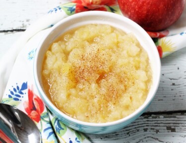 Applesauce in a bowl with two red apples on the side