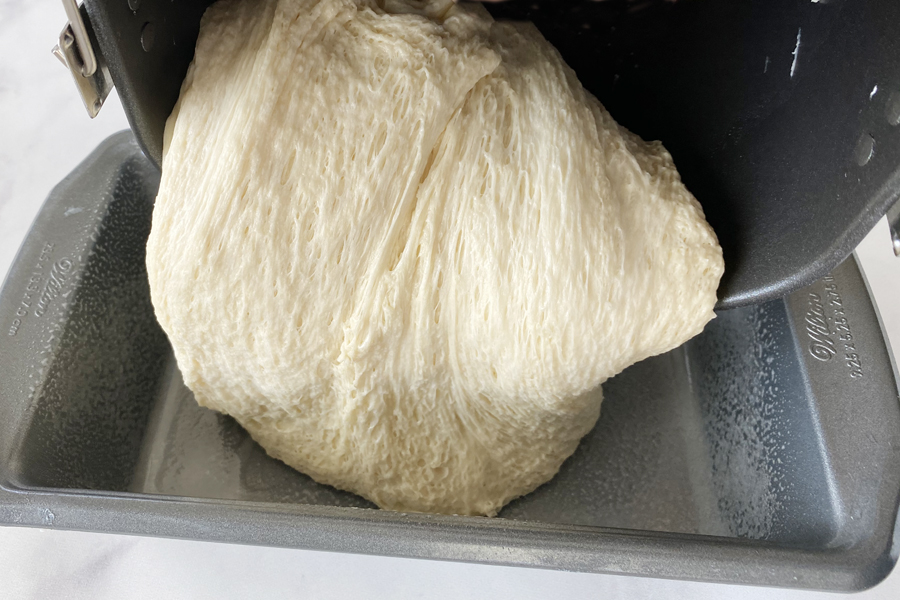 Bread machine dough being poured into a bread pan