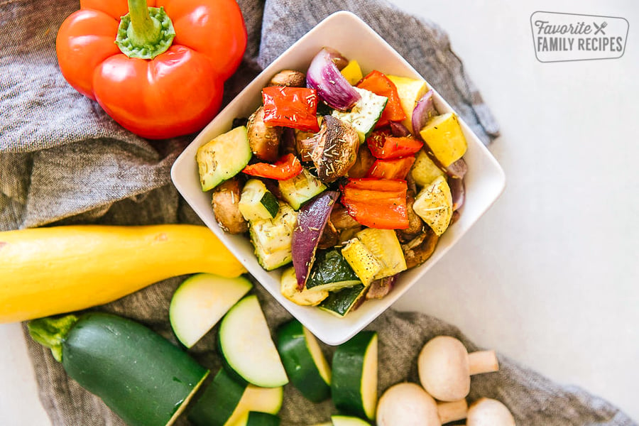 Oven roasted vegetables in a square dish with fresh vegetables on the side