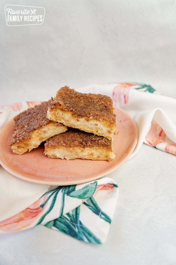 Made with crescent roll dough, these Sopapilla Cheesecake Bars are easy and quick to make. You'll love the layers of cinnamon sugar and sweet cream cheese. A stack of sopapilla cheesecake bars on a pink plate.