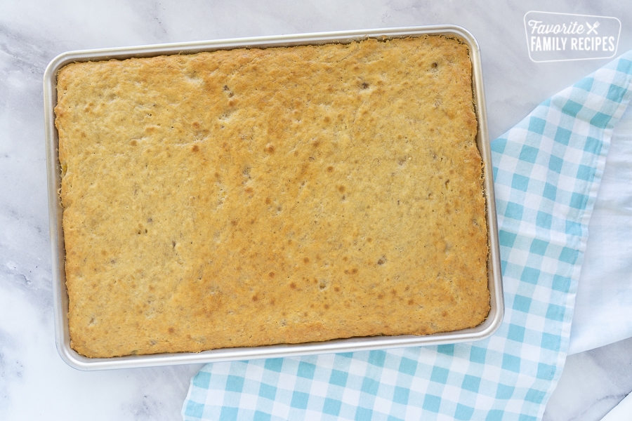 Banana Cake right before it is frosted with a blue and white checked napkin on a marble background.