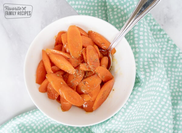 Sliced carrots in a white bowl with a spoon and a blue napkin