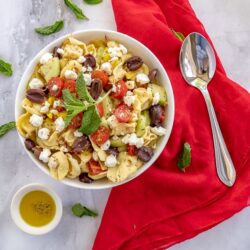 Overhead photo of Greek tortellini salad in a white bowl with a spoon on the side.