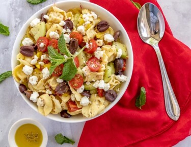 Overhead photo of Greek tortellini salad in a white bowl with a spoon on the side.