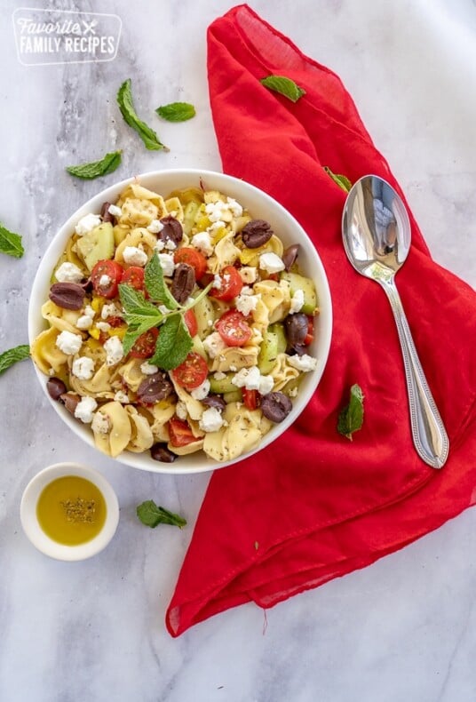 Overhead photo of Greek tortellini salad in a white bowl with a spoon on the side.