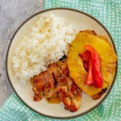 Chicken, pineapple, peppers, onion, and rice on a plate with a blue napkin and a marble background.