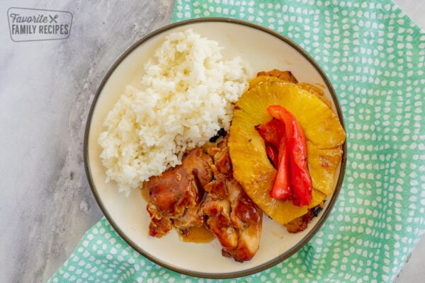 Chicken, pineapple, peppers, onion, and rice on a plate with a blue napkin and a marble background.