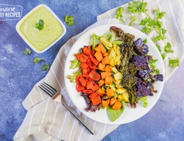 rainbow buddha bowl with creamy avocado dressing on a blue background with a fork.