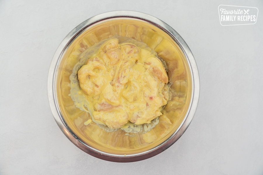 Chicken tenders dredged in batter in a silver bowl.