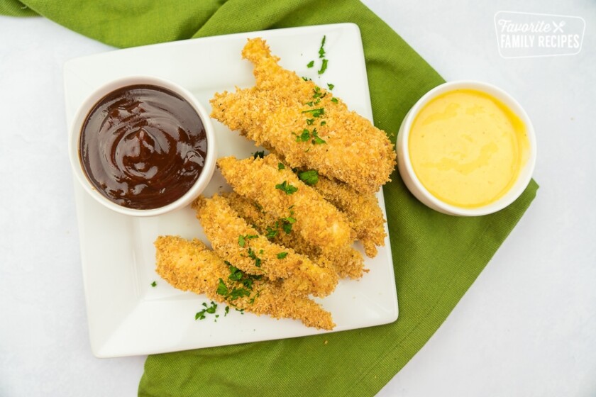 Baked chicken tenders on a plate with bbq and honey mustard dipping sauces.
