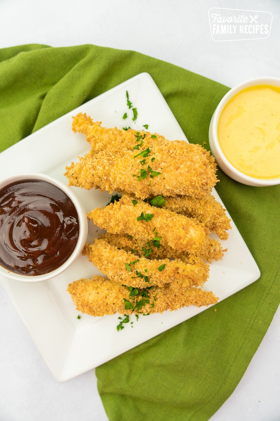 A pile of baked chicken tenders on a plate with little bowls of bbq sauce and honey mustard