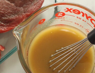 Homemade steak marinade in a pyrex glass measuring cup with a whisk.