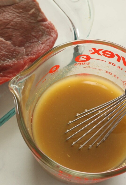 Homemade steak marinade in a pyrex glass measuring cup with a whisk.