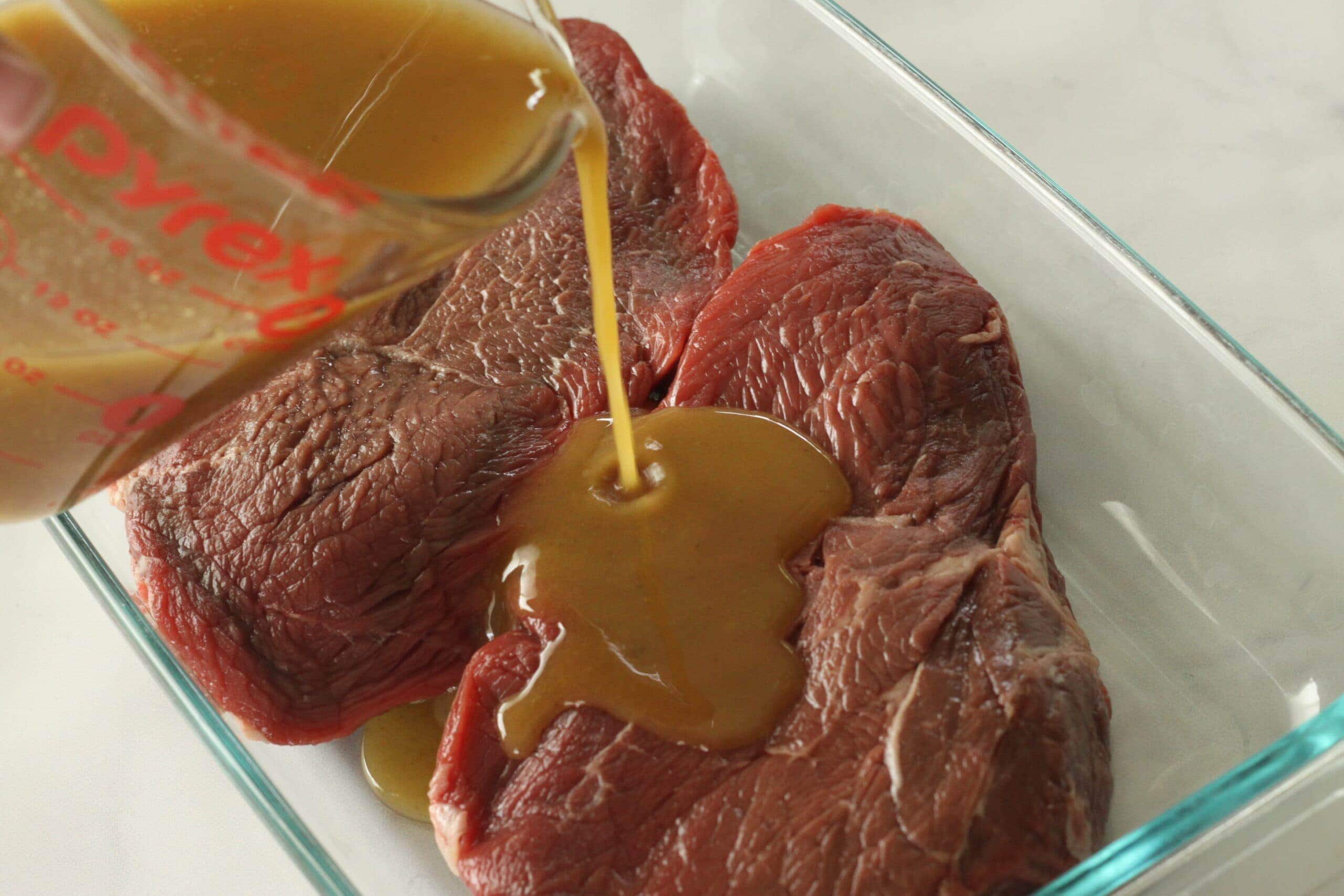 Steak marinade being poured over steak.