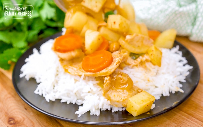 Chicken massaman curry on rice on a black plate.