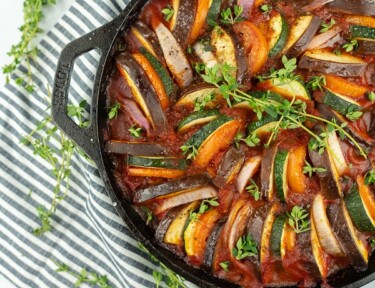 Ratatouille in a black skillet sitting on top of a striped tea towel.